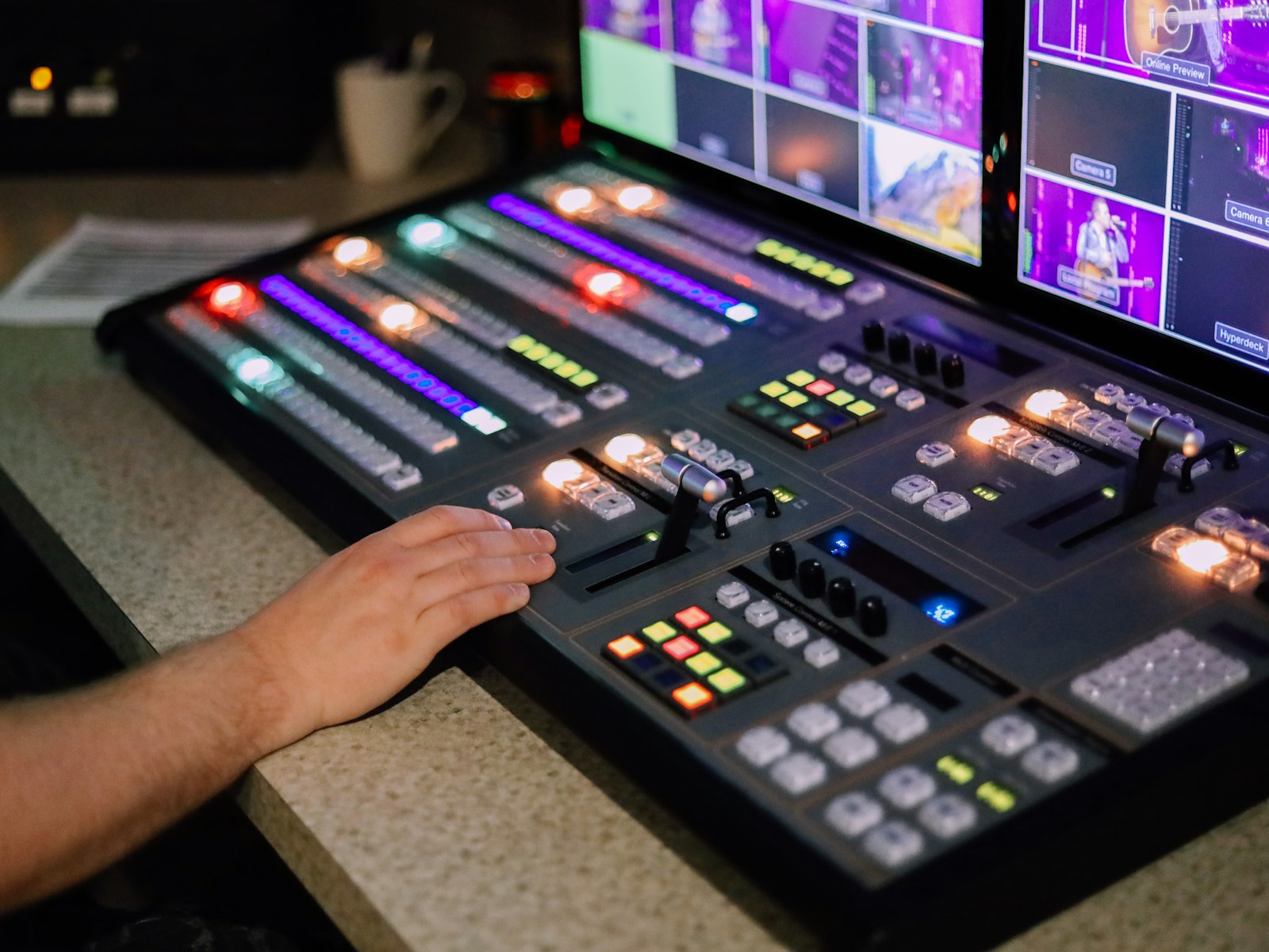 Hands on a video production switcher in front of a wall of monitors